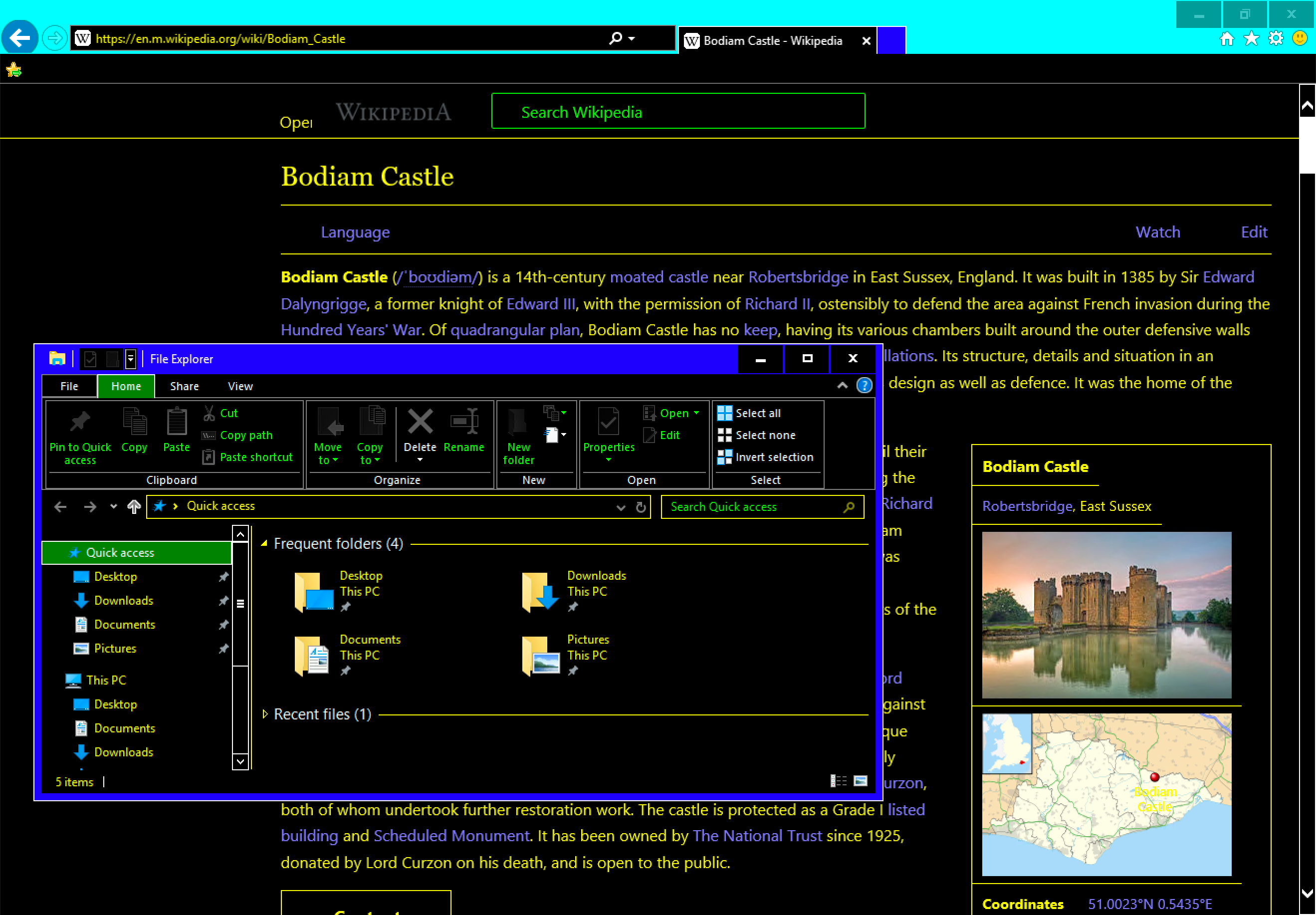 Screenshot of High Contrast Mode running on Windows 10. A Wikipedia page for Bodiam Castle is in the background, displayed in Internet Explorer 11. In the foreground is a window showing Window’s File Explorer. Content for both the Operating System UI and web content have been updated to display high contrast color values.