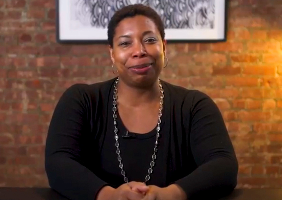 A video still of Reginé Gilbert smiling at the camera.